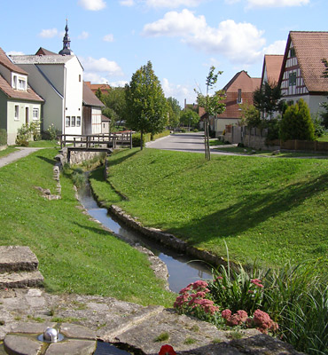 Mit Fördermitteln der Dorferneuerung hat Markt Nordheim den Geroldsbach neuge-staltet. Zu sehen ist ein Dorfkern mit Bach.