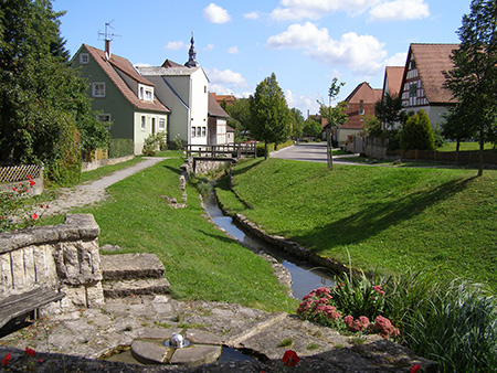Das Foto zeigt mit Fördermitteln der Dorferneuerung hat Markt Nordheim den Geroldsbach neugestaltet. Zu sehen ist ein Dorfkern mit Bach.